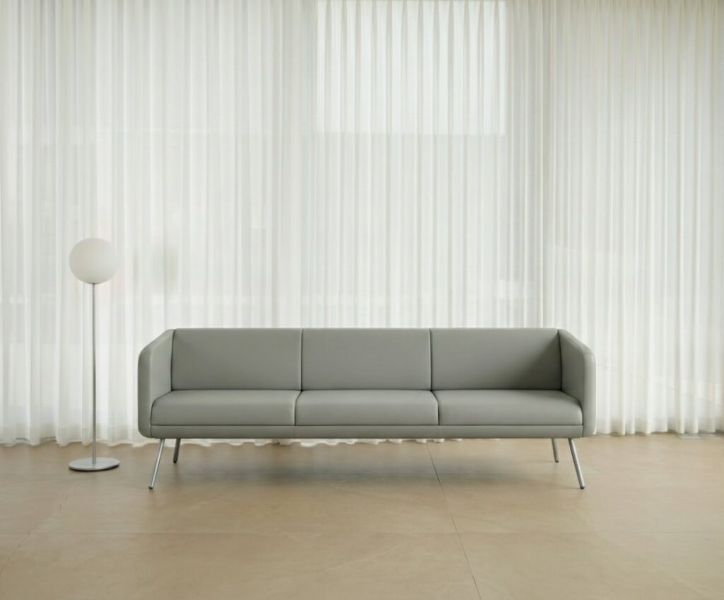 Set — Grey three-seater waiting sofa with metal legs, in a room with white sheer curtains, with a globe lamp on the floor