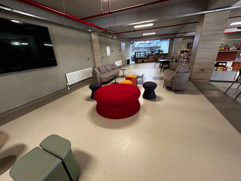 Lounge girişi, kırmızı puf ve duvara asılı ekran