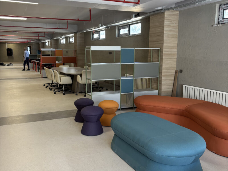 Lounge alanı, renkli puflar ve modüler raf sistemi
