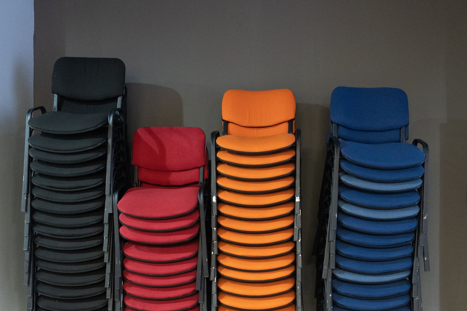 Stacks of colorful chairs neatly arranged against a gray wall indoors.